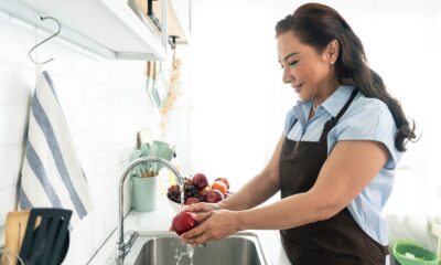 Happy smiling asian older woman in apron washing the apple in kitchen. housewife cooking concept.